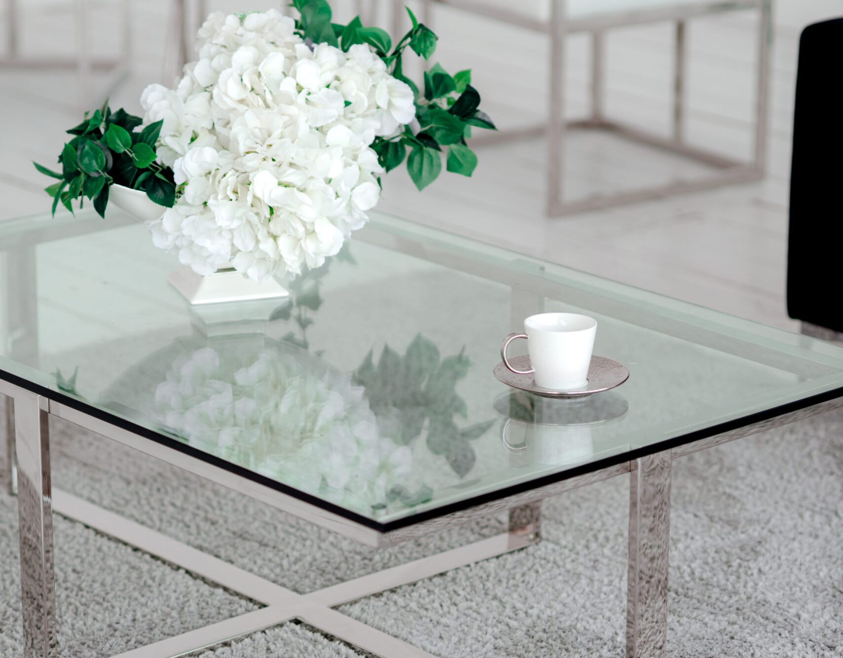 Fragment of a luxurious interior of a modern apartment. White wall, glass table, composition of white flowers and a navy sofa.